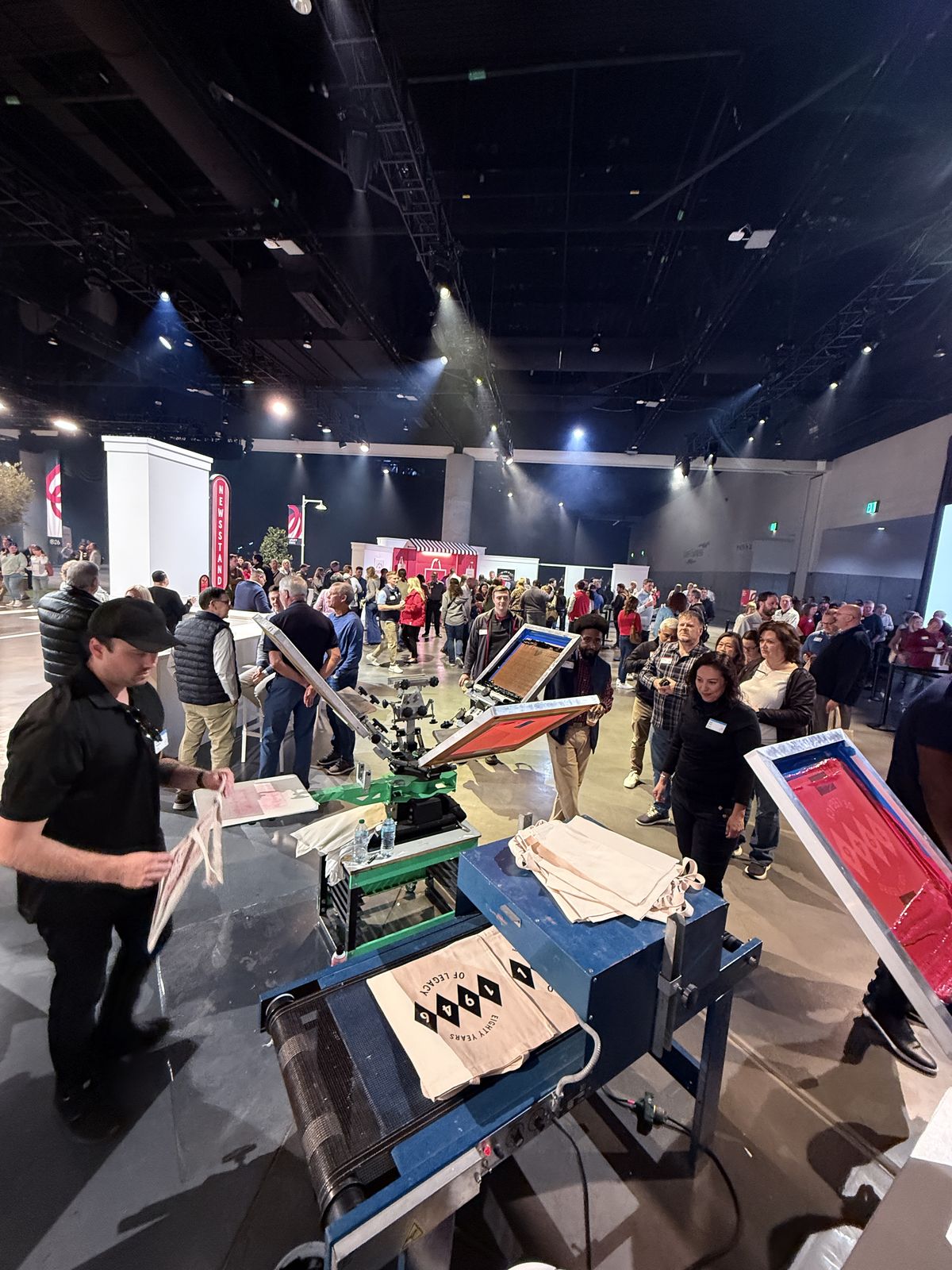 Wide view of a convention hall with live printing stations and a crowd of attendees